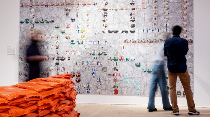 Illustrerad karta över London, hänger som en stor tavla på vägg, personer med ryggen åt kameran tittar på kartan, Upphovsman: Konstnär Lars Arrhenius