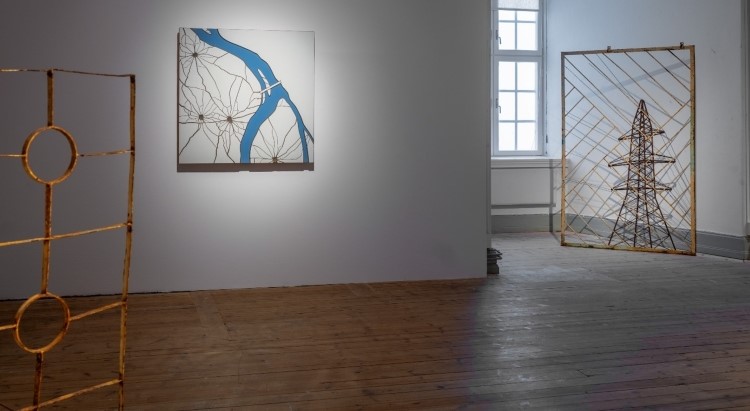 Del av grind i förgrunden. Sönderskjuten kakelplatta hänger på väggen. 